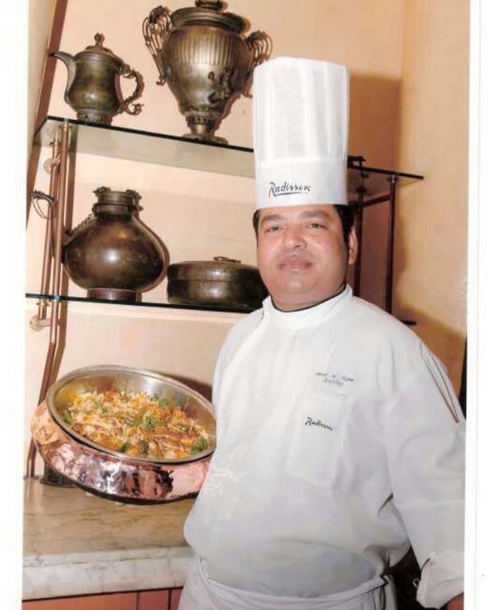 Chef Meraj Ul Haque in Radisson chef whites beside a copper handi of dum biryani